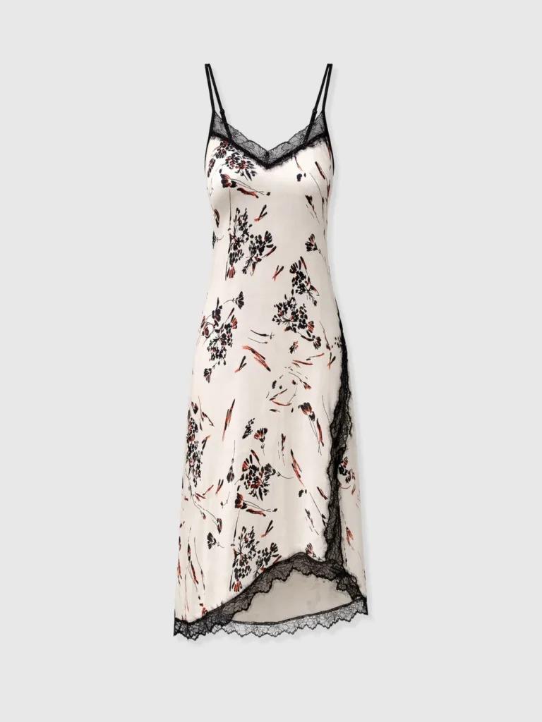 The Harper Lace Cami Dress from Saint and Sofia. A sleeveless midi with an asymmetric hem and floral lace detailing along the trims. It has a white and black floral print with pops of orange.