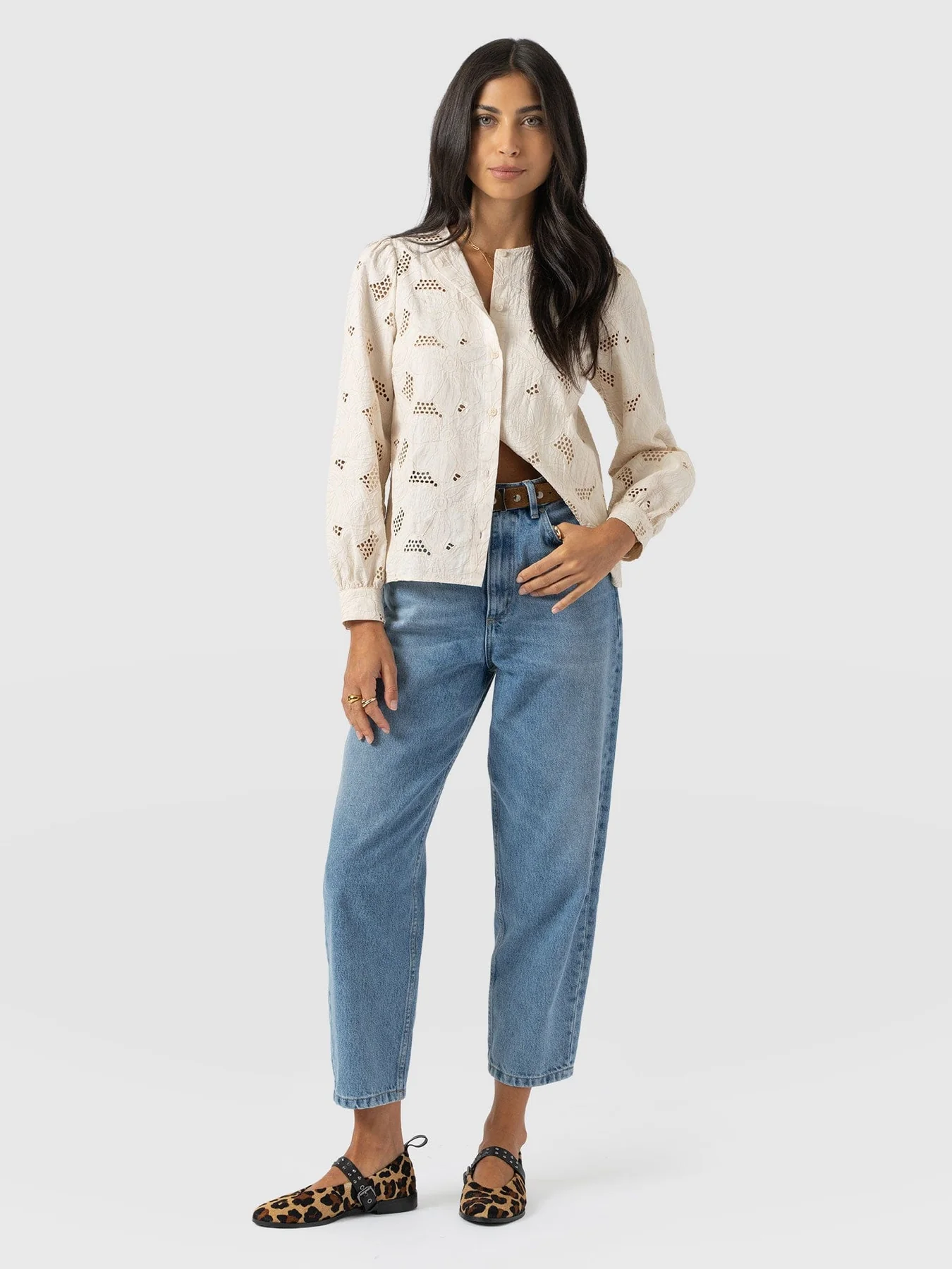 A model wearing the Tabitha Blouse in Cream Floral by Saint and Sofia. A long sleeved blouse with a buttoned up fastening, crew neckline, and buttoned cuffs. It features floral embroidery with cut out detailing.